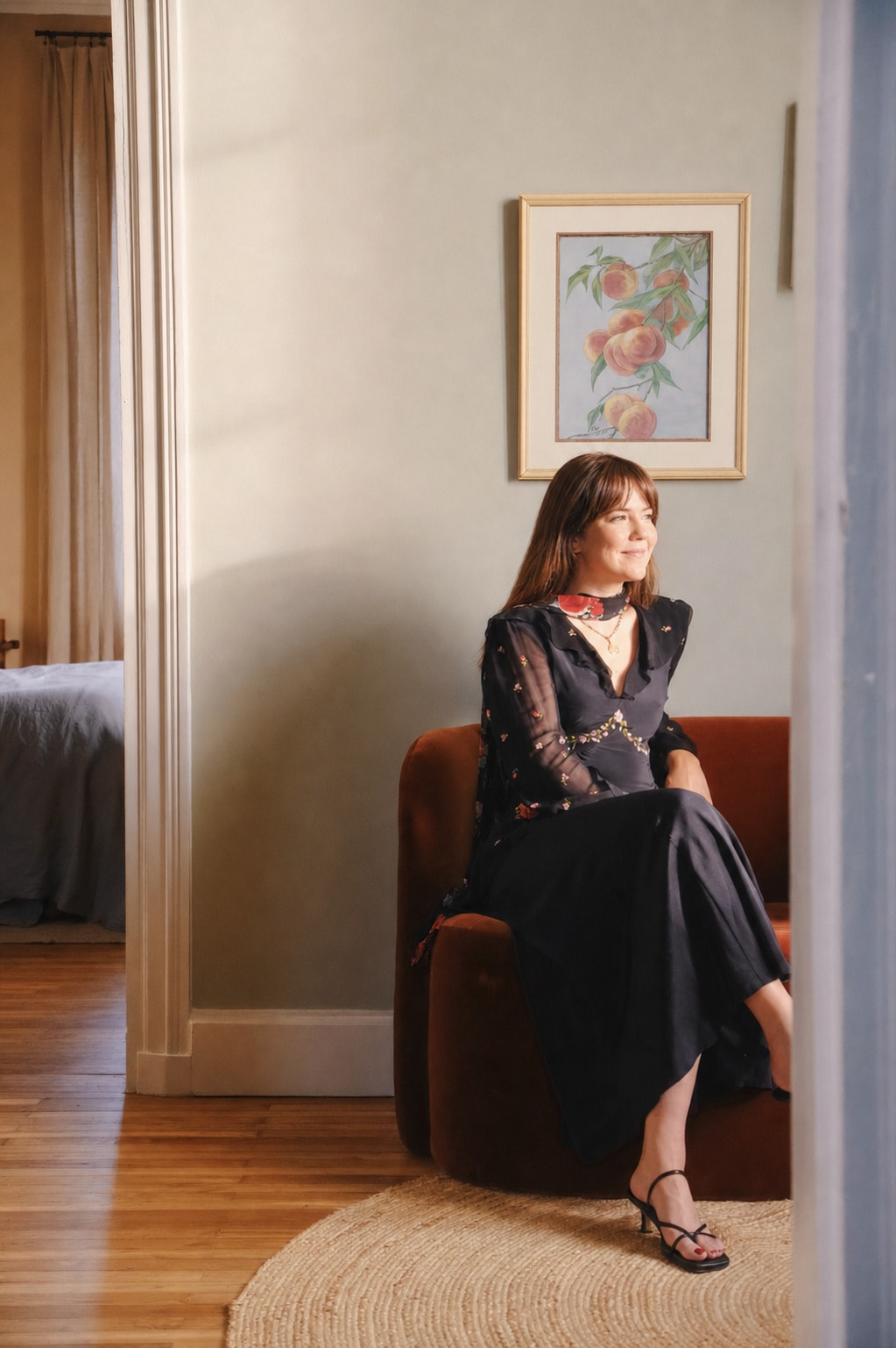 Bianca seated in a terracotta armchair beside a framed still life