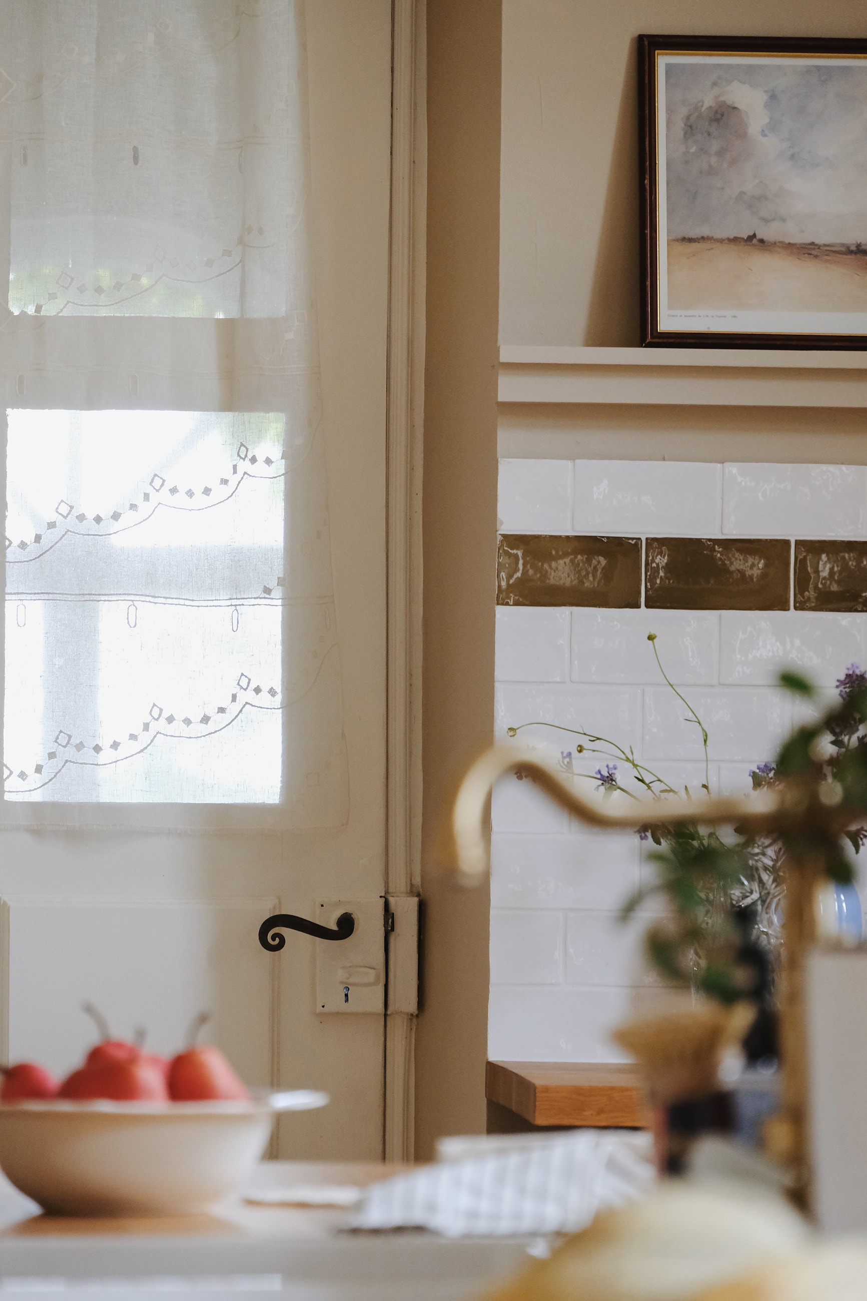 Kitchen detail with an embroidered blind, olive tiled border and brass tap
